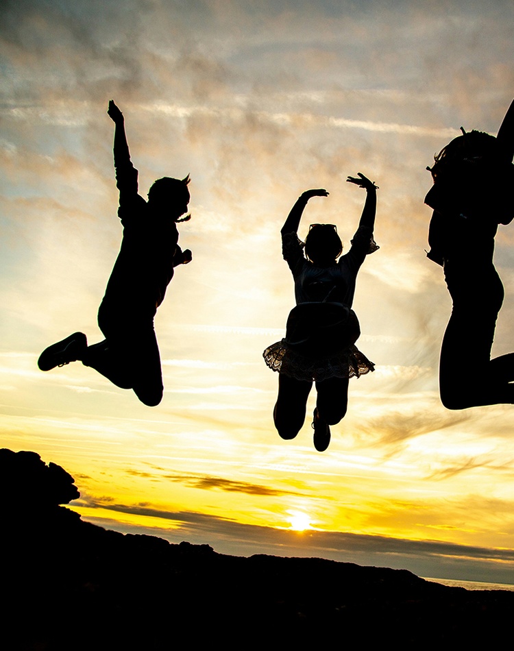Teenagers jumping against sunset sky