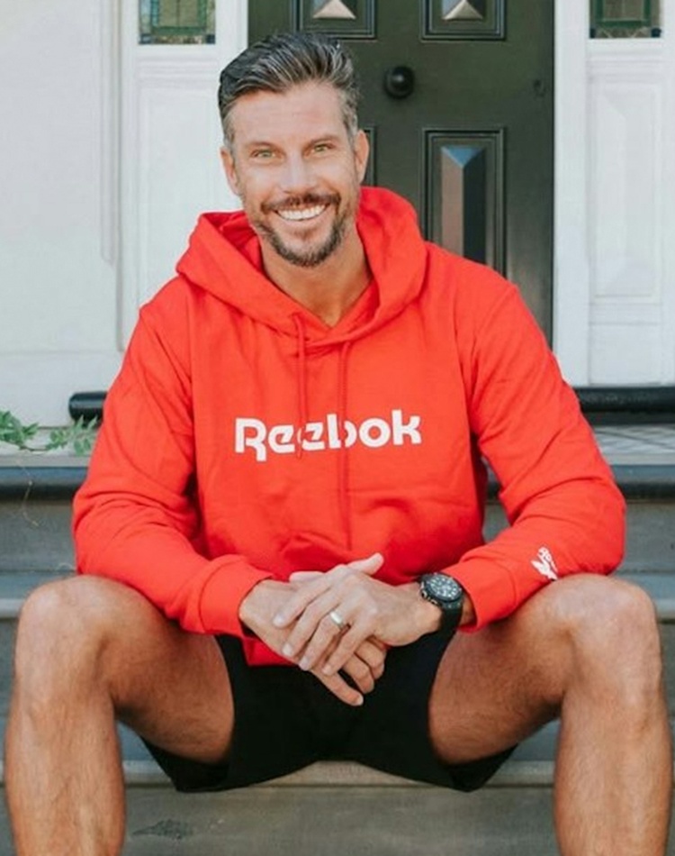 A man with a beard sitting on a set of stairs wearing a red hoodie