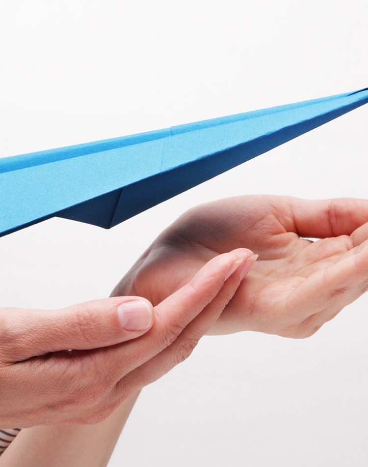 blue paper plane lifting off hands into the air