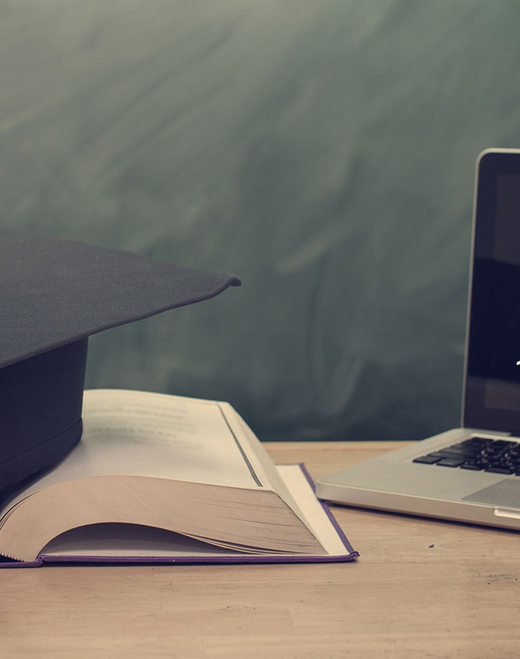 computer screen on a desk with a mortar board graduate hat on top of a book