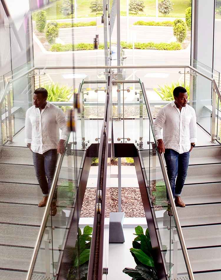 Dieudonne Ininahazweis a Psychology Alumnus he is walking down some stairs next to a glass wall which is reflecting the image