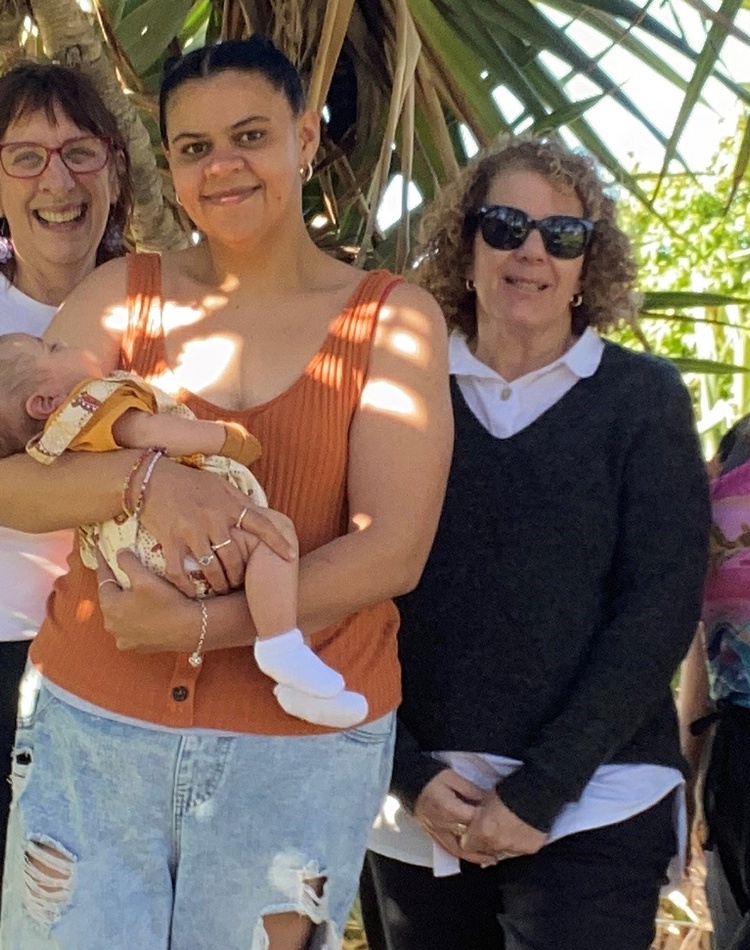 A group of women in front of a pandanus tree, with one of them holding a baby