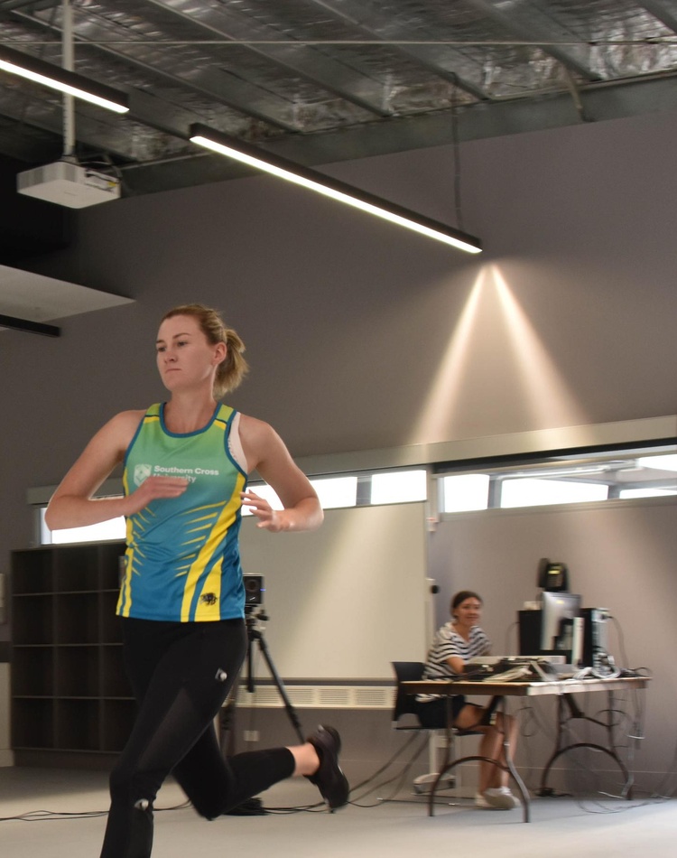 A health sciences student is running in the foreground , she is being fitness testing by another health sciences student in the background at the southern cross university coffs harbour campus