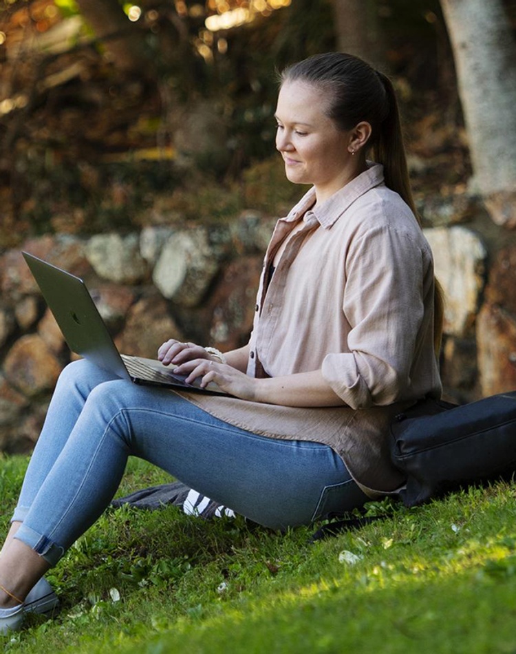Female student sitting on grass with laptop in afternoon sun