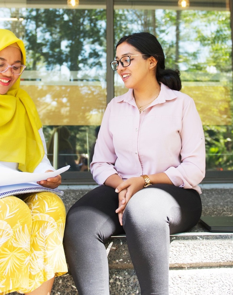 Two students sit together and chat.