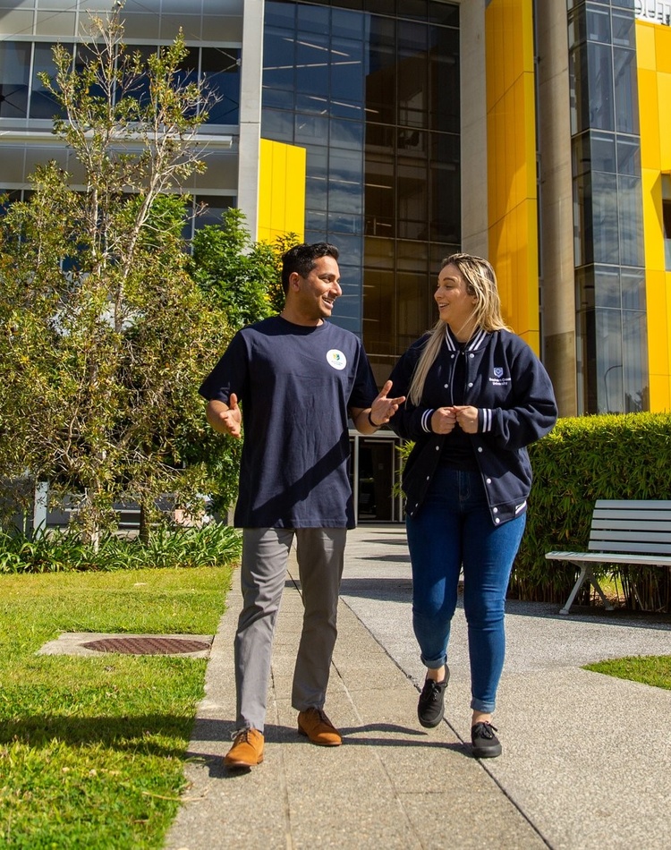 Two students talk side-by-side while walking through Gold Coast campus.