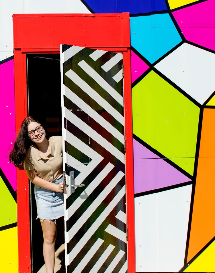 A student pokes her head out of a door set into a mural at the Southern Cross University Lismore campus