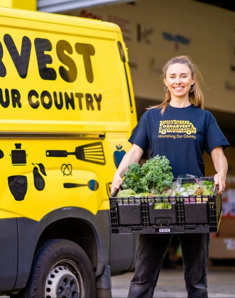 OzHarvest food volunteer stands beside a yellow delivery truck