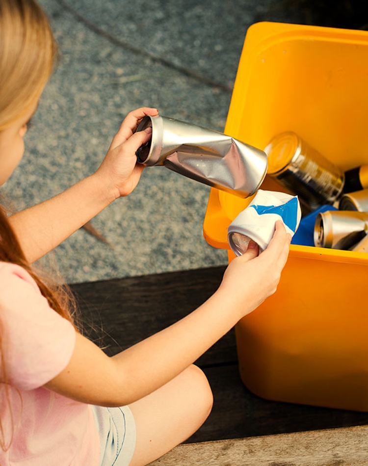 Young girl recycling cans into bin
