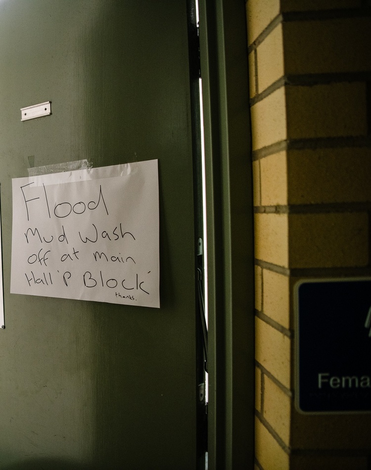 A sign on a bathroom door reads 'Wash flood mud off at Main Hall P Block'