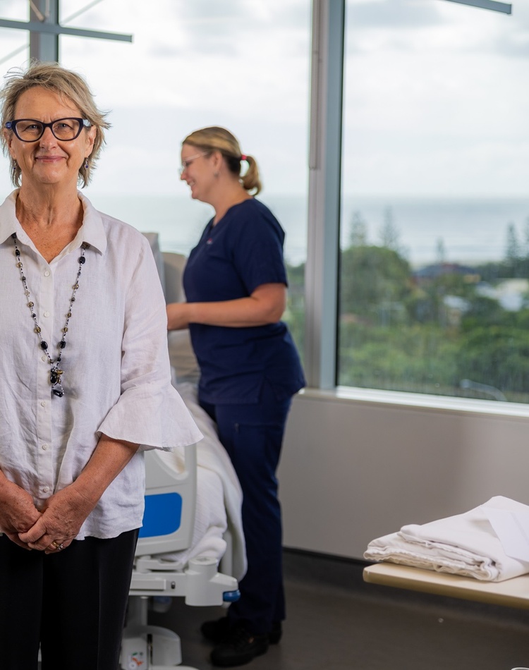 A woman smiling at the camera, hospital setting in the background