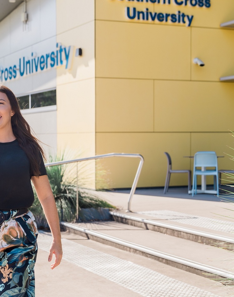 A woman walking away from a yellow fronted building with Southern Cross University logo