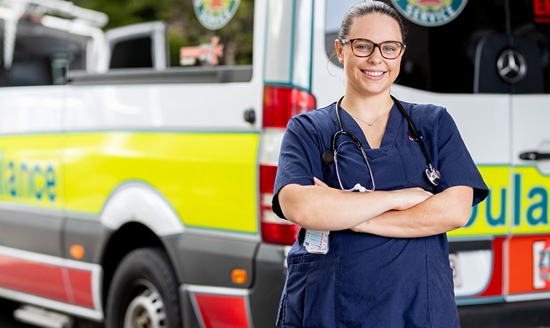 Ashleigh Woods stands in front of an Ambulance wearing her blue Nursing uniform and stethoscope