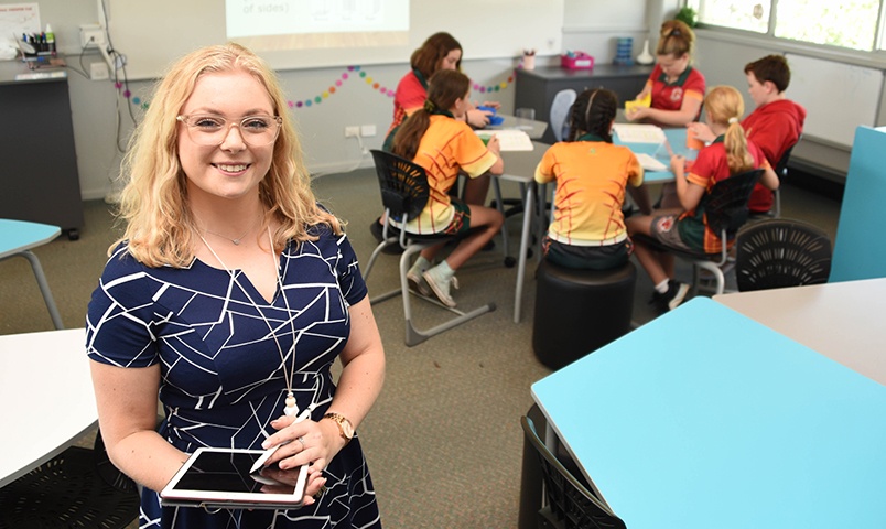 Holly Wedd stands in a classroom at South Grafton High School with a group of five children gathered around a school table working through maths problem