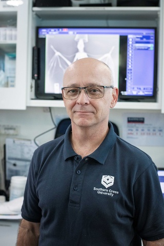 Man with glasses looking to camera in veterinary clinic with bird x-ray in background