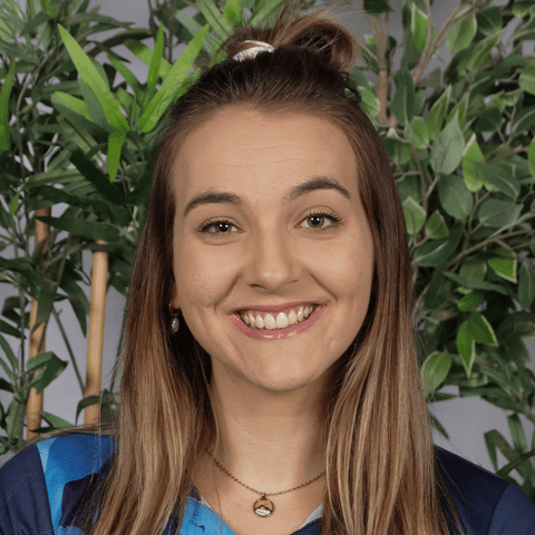 Headshot of woman with long hair and greenery in background