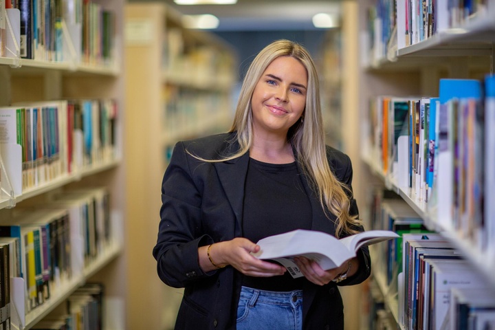 Student holding open book in library