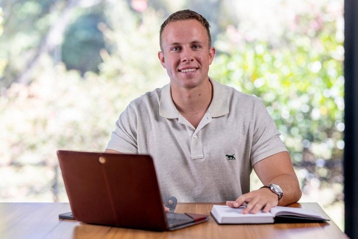Student smiling at camera with laptop and book
