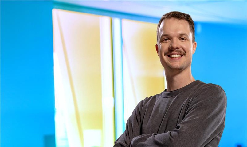 Man in grey jumper smiling with arms crossed