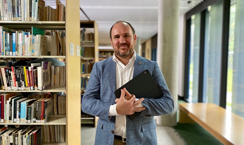 A man in suit holding a laptop in a library