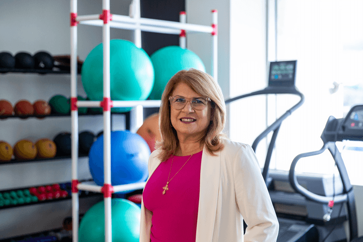 Maria smiling at camera with exercise balls and treadmill in background