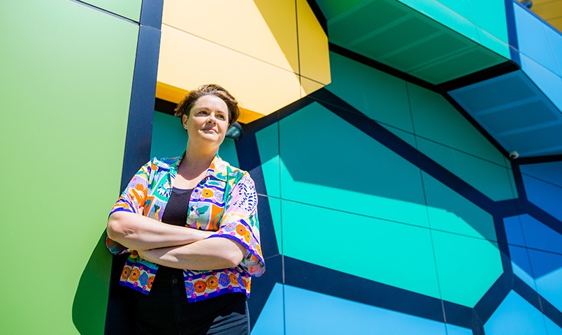 Cecile Knight Exhibitions Officer at Home of the Arts (HOTA) and SCU graduate stands outside the brightly coloured walls at HOTA wearing a bright coloured shirt