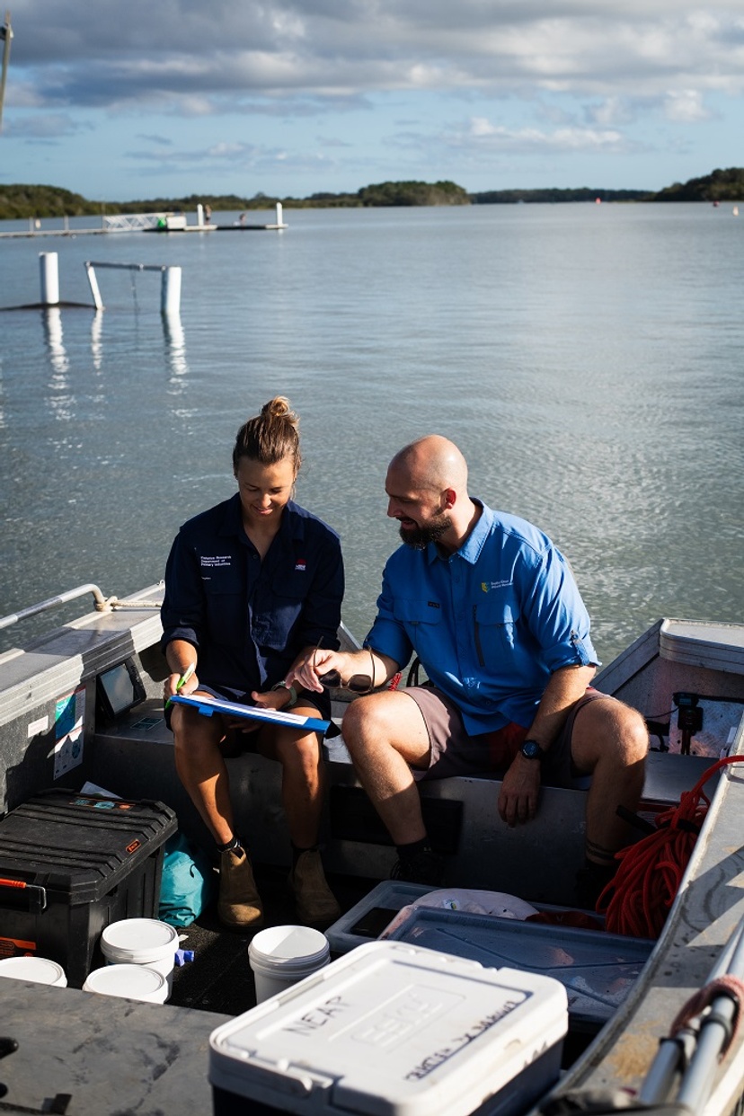 Two people in a stationary boat discussing test results, buckets and testing equipment around them