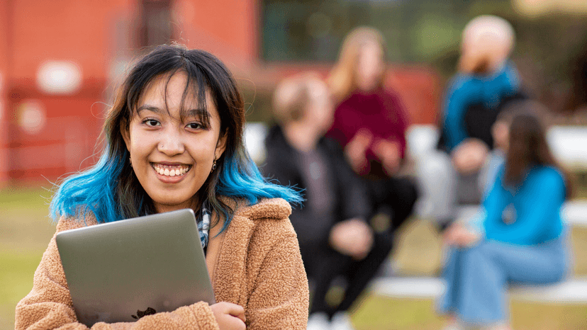 Student in foreground smiling at Lismore campus with students blurred in background