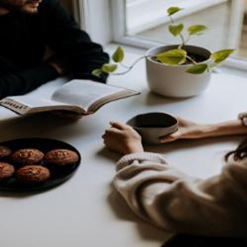 Two people sitting at a table with a book and coffee