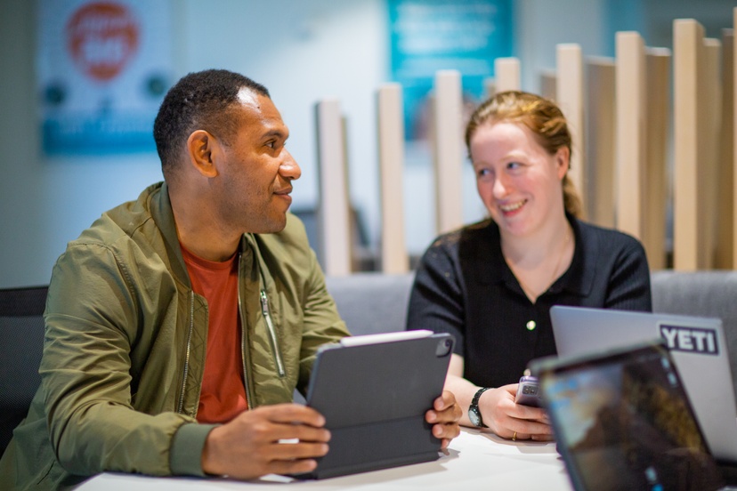 Two students chat in front of computers.