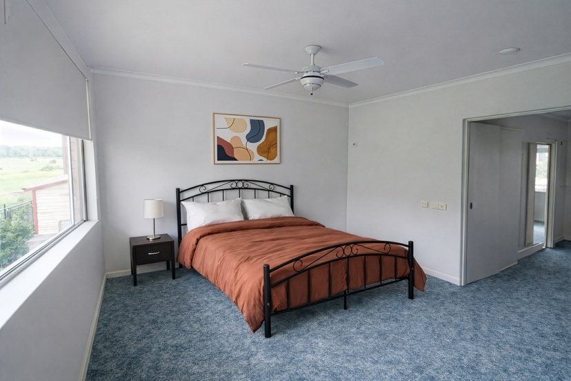 Bedroom with large bed, orange covers and art on the walls and natural light from window