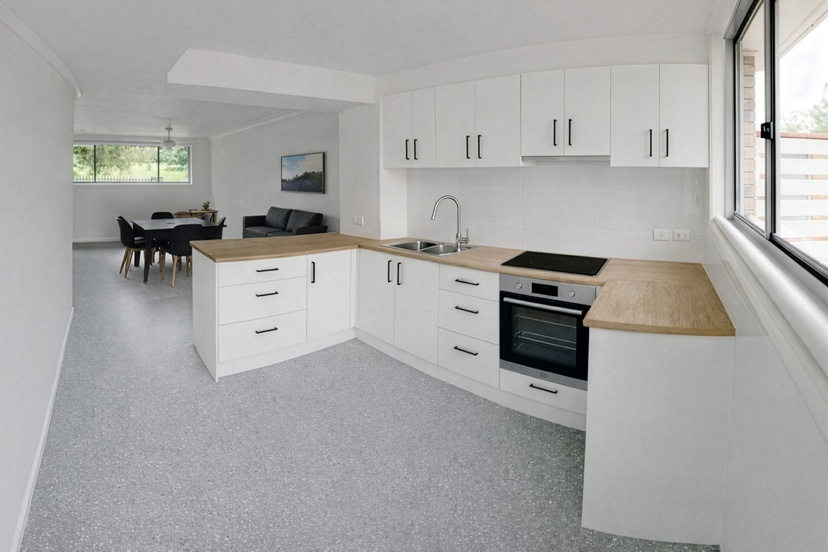Open plan white kitchen with wooden countertops, oven, washing machine and open plan into lounge