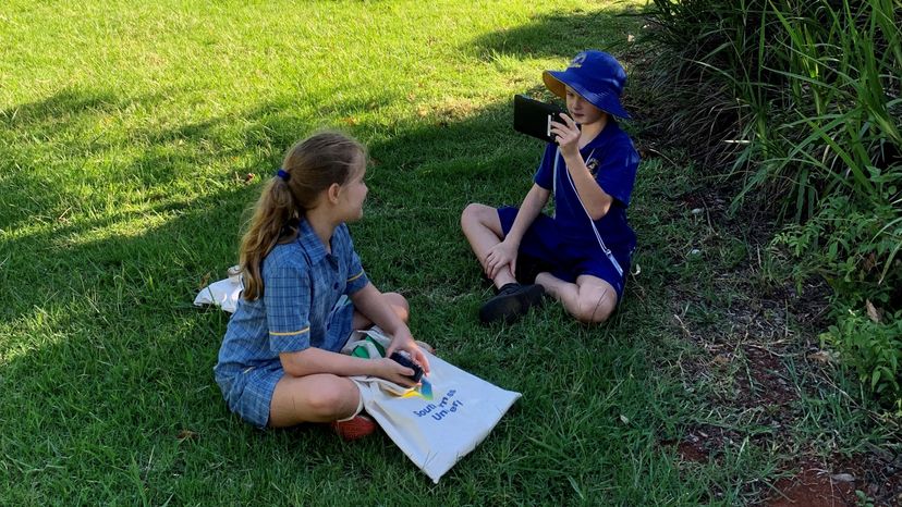 Two children sitting on grass talking and learning
