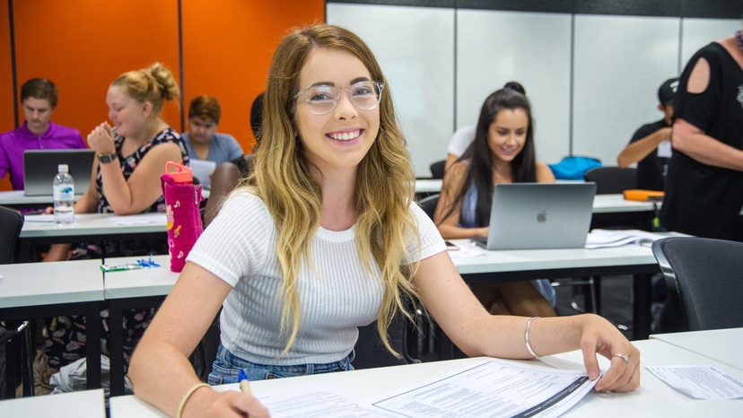 Female student with glasses sitting in classroom with other students in background