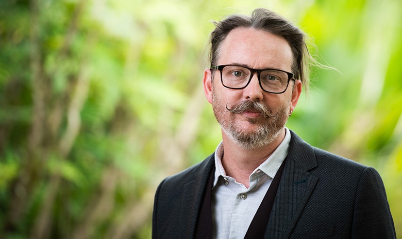 Professor Thomas Roche, Pro Vice-Chancellor for Academic Quality looks at camera with greenery behind him, wearing glasses and a suit