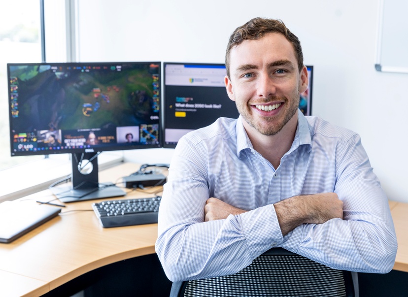 Dr Dylan Poulus smiles to camera in front of a computer screen