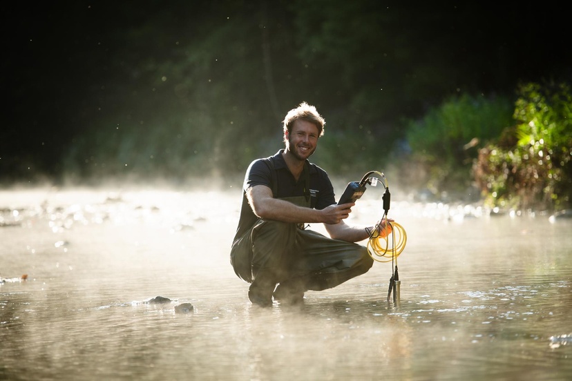 Scientist in overalls crouched in creek with equipment