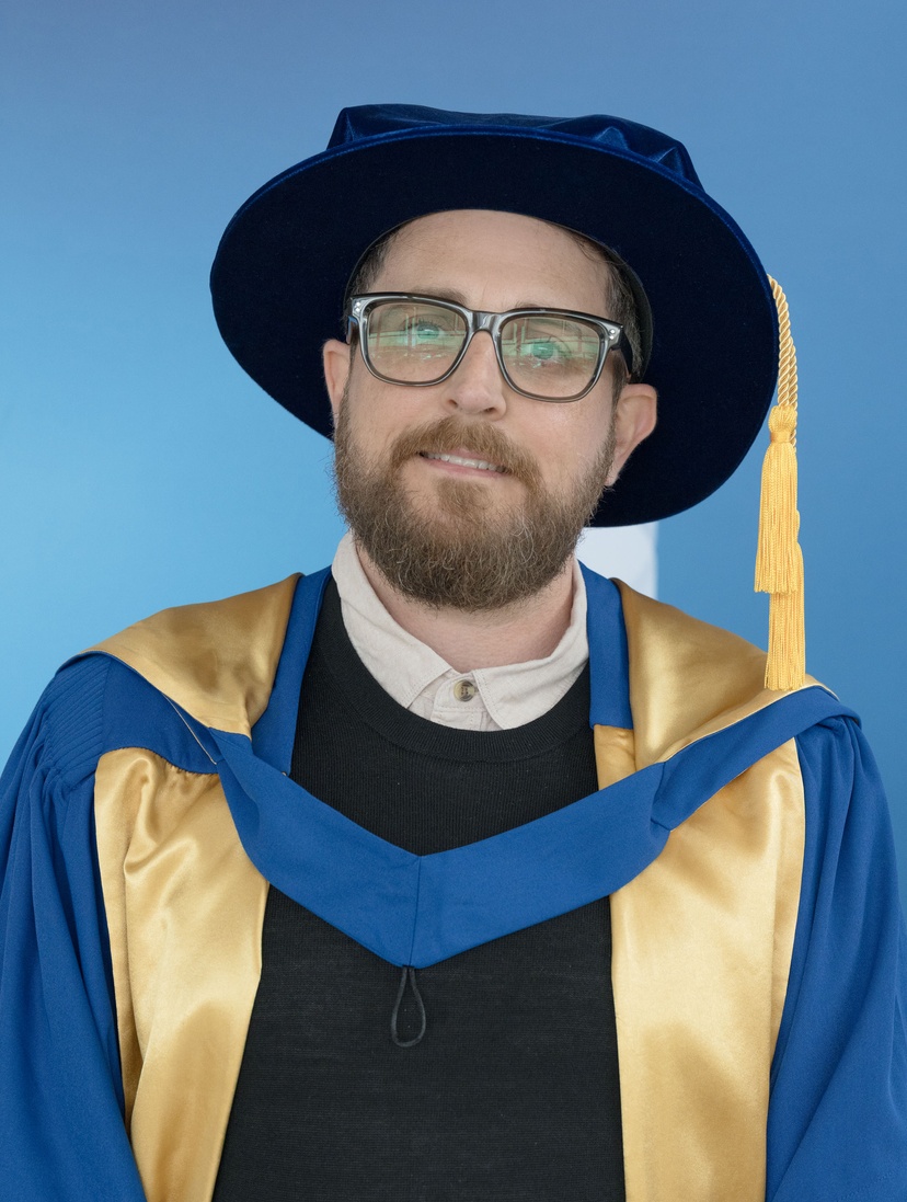 Man in graduation robe and cap with blue background