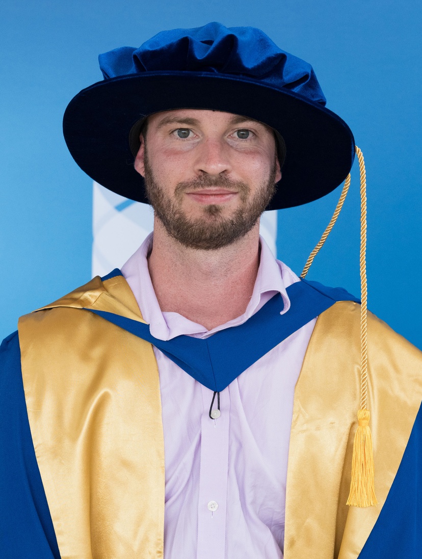 Male in graduation robe and cap with blue background