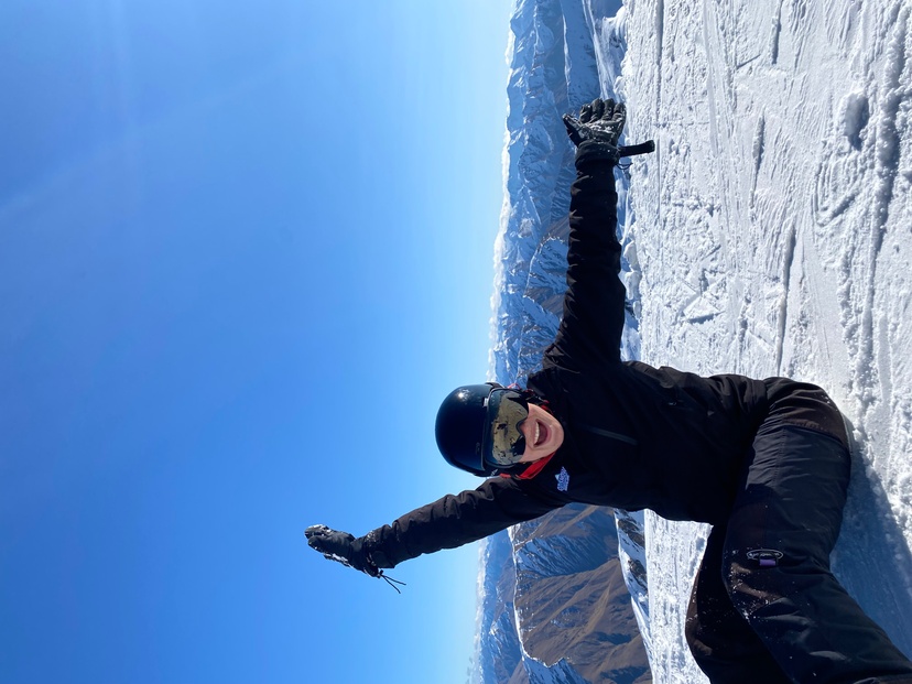 Female in snow gear sitting on snow with mountain behind