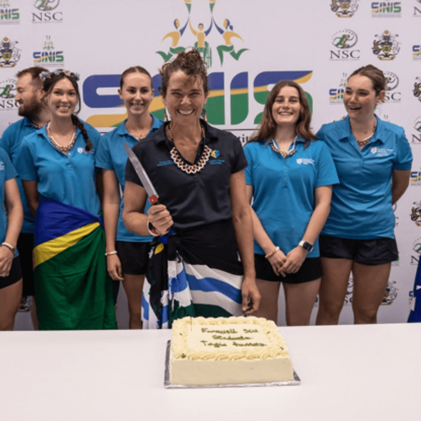A woman holds a cake-cutting knife in front of a cake and a group of students