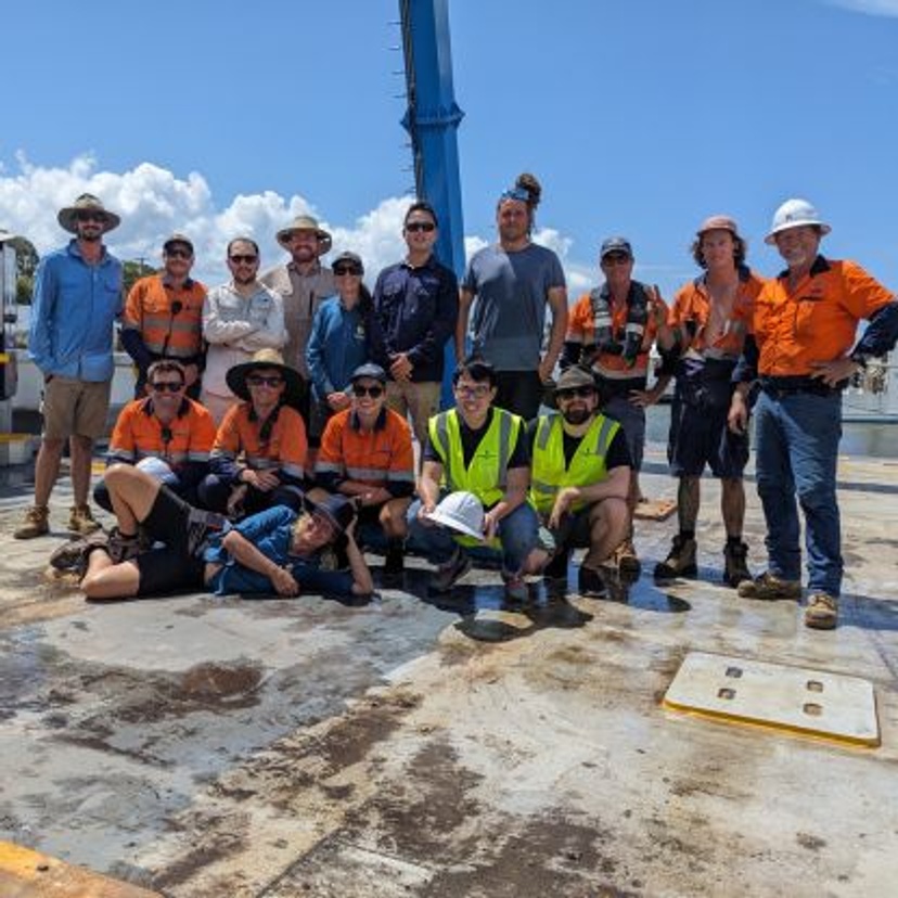 Large group of people in high vis workwear smiling at camera on board a large boat