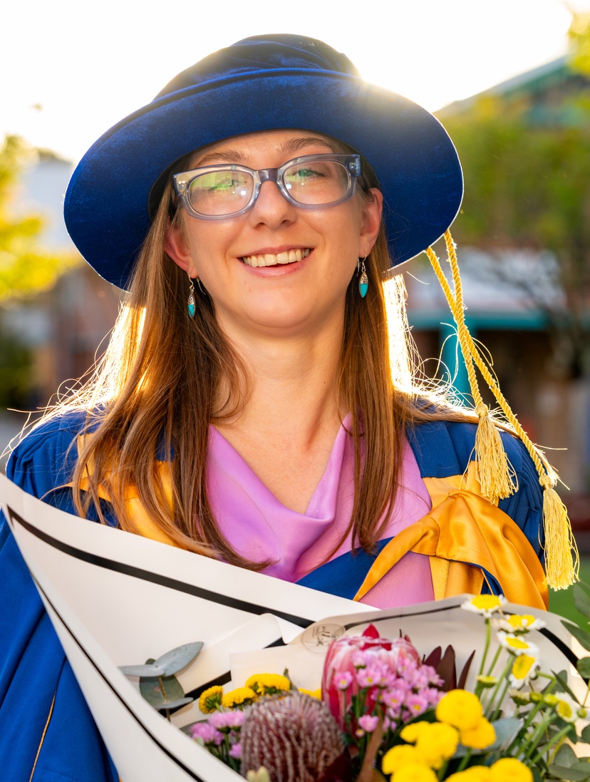 Female outside in graduation robe and gown with flowers