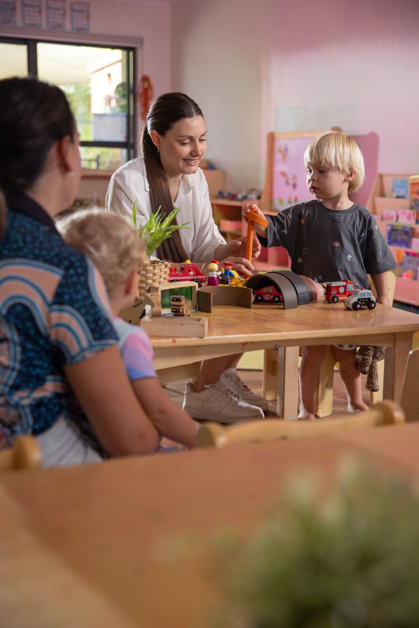 childcare educator smiling and playing with blonde bot in clasrrom