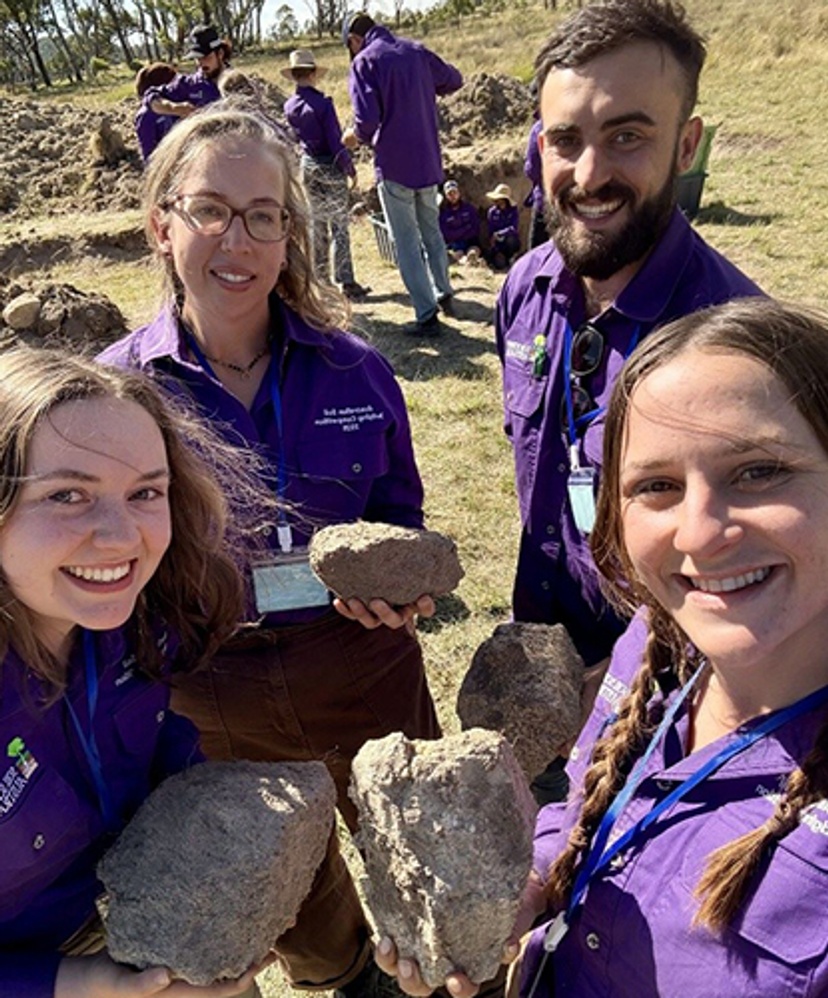 Three women one male smiling at the camera holding rocks