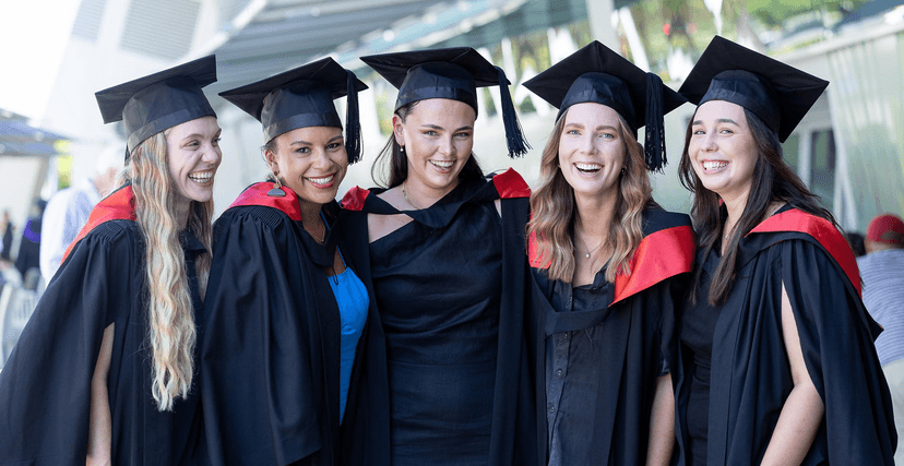 Group of students in graduation robes and mortarboards smiling at camera