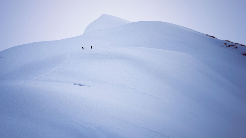 Two mountain climbers in distance climbing snowy mountain