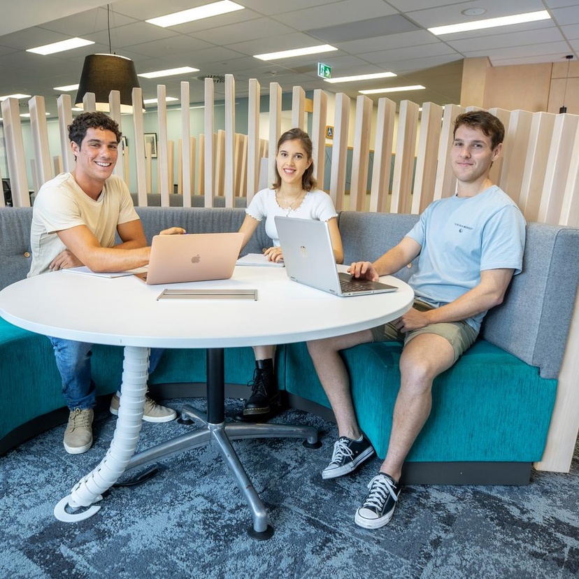 3 university students sitting at round white table looking at camera