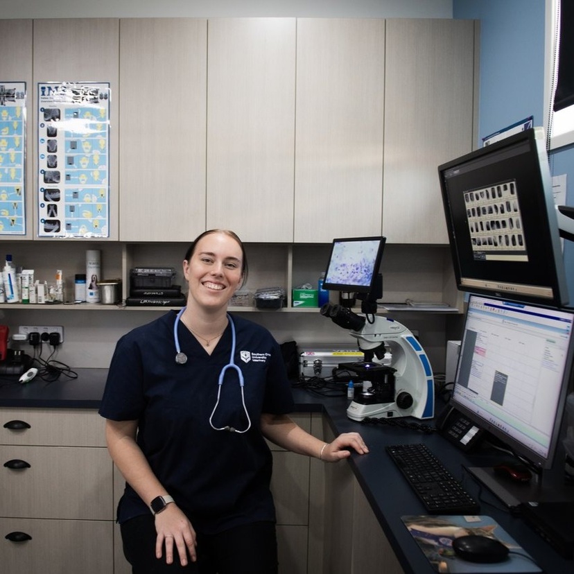 person wearing scrubs in a lab, looking and smiling at camera