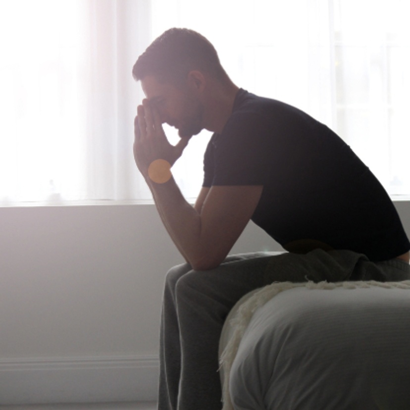 Man sitting on a bed with his head in his hands